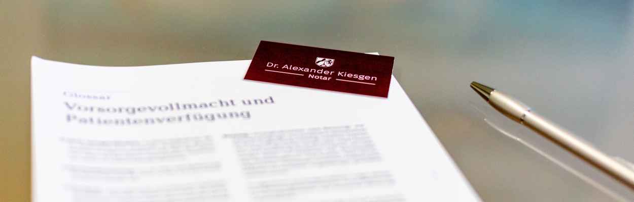 Eine Visitenkarte von Dr. Alexander Kiesgen, ein Kugelschreiber und ein Formular unscharf im Vordergrund